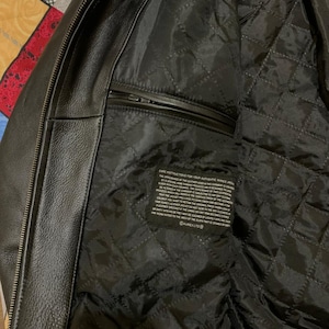 May include: Black leather jacket with a quilted black lining. The jacket has a zipper closure and a small pocket on the inside. The care instructions are printed on a tag inside the jacket.