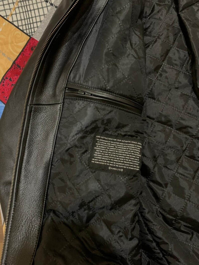 May include: Black leather jacket with a quilted black lining. The jacket has a zipper closure and a small pocket on the inside. The care instructions are printed on a tag inside the jacket.