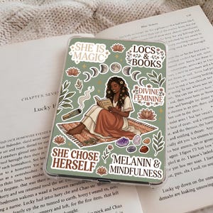 May include: A rectangular tablet case with a sage green background featuring a central illustration of a person reading a book on a rug. Text includes SHE IS MAGIC, LOCS & BOOKS, DIVINE FEMININE, SHE CHOSE HERSELF, and MELANIN & MINDFULNESS.