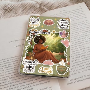 May include: A phone case with a design featuring a woman reading a book, surrounded by botanical illustrations and stickers with phrases like "black girl magic" and "I am enough."