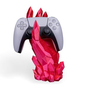 May include: A white and black games controller is displayed on a bright red crystal stand. The stand is made of multiple, sharp crystal formations. The controller has a symmetrical button layout and a central touchpad.