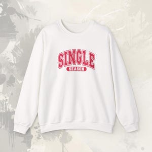 Puede incluir: Una sudadera blanca con las palabras "SINGLE SEASON" en letras rojas en el pecho. La sudadera tiene cuello redondo y mangas largas. El texto está en una fuente de estilo universitario.