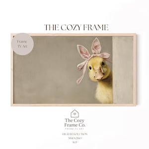 May include: A framed digital art print showing a yellow duckling wearing a pink bow with bunny ears. The duckling peeks from behind a wall. The text "THE COZY FRAME" is at the top. The Cozy Frame Co. logo is at the bottom.
