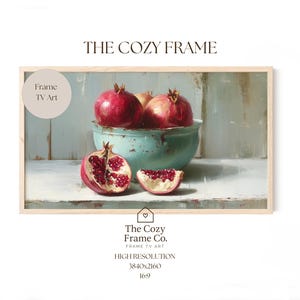 Peut inclure: Impression numérique encadrée représentant une nature morte de grenades. L'image montre des grenades entières et coupées dans un bol turquoise. Le texte "THE COZY FRAME" est en haut. The Cozy Frame Co. est en bas.