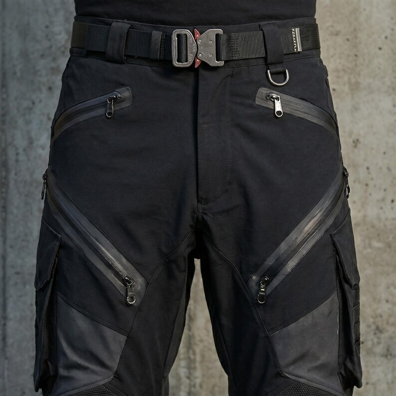 May include: Black tactical cargo pants featuring multiple slanted zippered pockets, reinforced panels on the thighs, and a heavy-duty black nylon belt with a metallic quick-release buckle. The design includes integrated D-ring attachments.