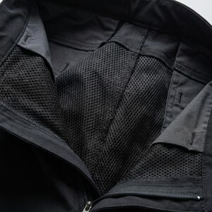 May include: Black trousers featuring a solid fabric exterior and a black mesh lining visible at the open waist area. The garment includes a zippered fly closure, reinforced stitching along the seams, and a structured waistband with belt loops.
