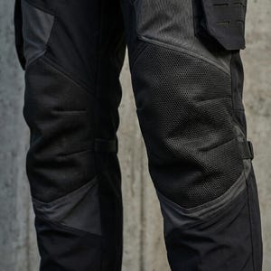 May include: Black and dark gray tactical pants featuring reinforced mesh panels over the knees, integrated side pockets with laser-cut MOLLE webbing, and adjustable straps on the sides for a secure fit, constructed from durable technical fabric.