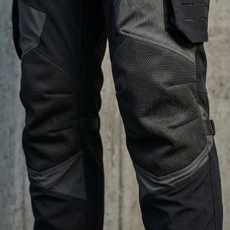 May include: Black and dark gray tactical pants featuring reinforced mesh panels over the knees, integrated side pockets with laser-cut MOLLE webbing, and adjustable straps on the sides for a secure fit, constructed from durable technical fabric.