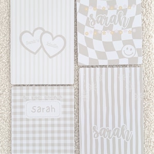 Peut inclure: Quatre cahiers personnalisés avec des motifs beige clair et blancs. L'un présente un motif à carreaux avec le nom "Sarah" et des smileys. Un autre présente le nom "Sarah" en script. Les deux autres ont des cœurs et des rayures, avec le texte "Sarah's Kindle" et "This Kindle belongs to Sarah".