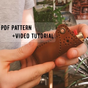 May include: A brown leather lighter case with decorative stitching and a brass grommet. The text "PDF PATTERN + VIDEO TUTORIAL" is overlaid on the image. The lighter has a gold-colored metal body and a red ignition button.