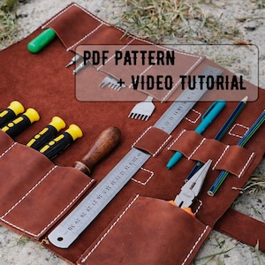 Può includere: Un rotolo di attrezzi in pelle marrone con vari strumenti, tra cui cacciaviti, un righello e pinze. Il rotolo è aperto, mostrando gli strumenti nelle loro tasche. Il testo "PDF PATTERN + VIDEO TUTORIAL" è visibile. Il rotolo è fissato con due fibbie metalliche.