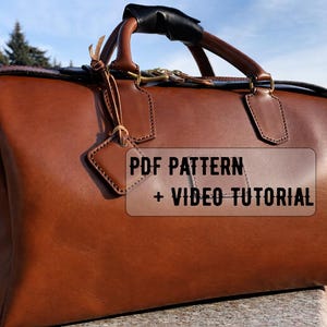May include: A brown leather duffel bag with a top handle and shoulder strap. The bag has a tag and the text "PDF PATTERN + VIDEO TUTORIAL" is visible on the front. The bag is sitting on a stone surface.