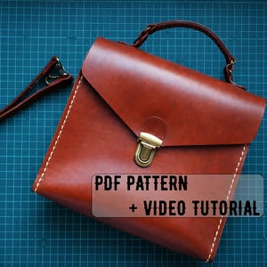 Pode incluir: Uma bolsa de couro marrom com uma alça superior e uma alça longa. A bolsa tem um fecho de aba com um fecho dourado. Costuras brancas acentuam as bordas. O texto na imagem diz "PDF PATTERN + VIDEO TUTORIAL".