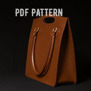 May include: A brown leather tote bag with a rectangular shape and a handle at the top. The bag has two long handles and gold-coloured hardware. The text "PDF PATTERN" is displayed at the top of the image.