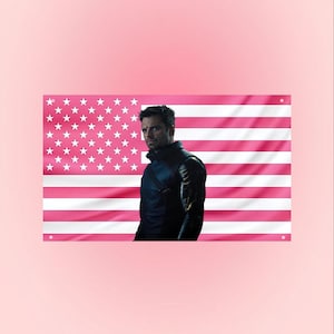 Puede incluir: Una bandera estadounidense rosa con estrellas y rayas blancas, con una persona con una chaqueta negra. La bandera es el telón de fondo y la persona está colocada a la derecha. El fondo es de color rosa liso.