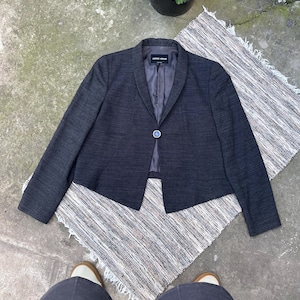 May include: A dark charcoal gray blazer with a textured fabric finish, featuring a single-button closure, a shawl collar, and long sleeves. The interior lining is a solid dark gray, and the garment label reads Giorgio Armani.