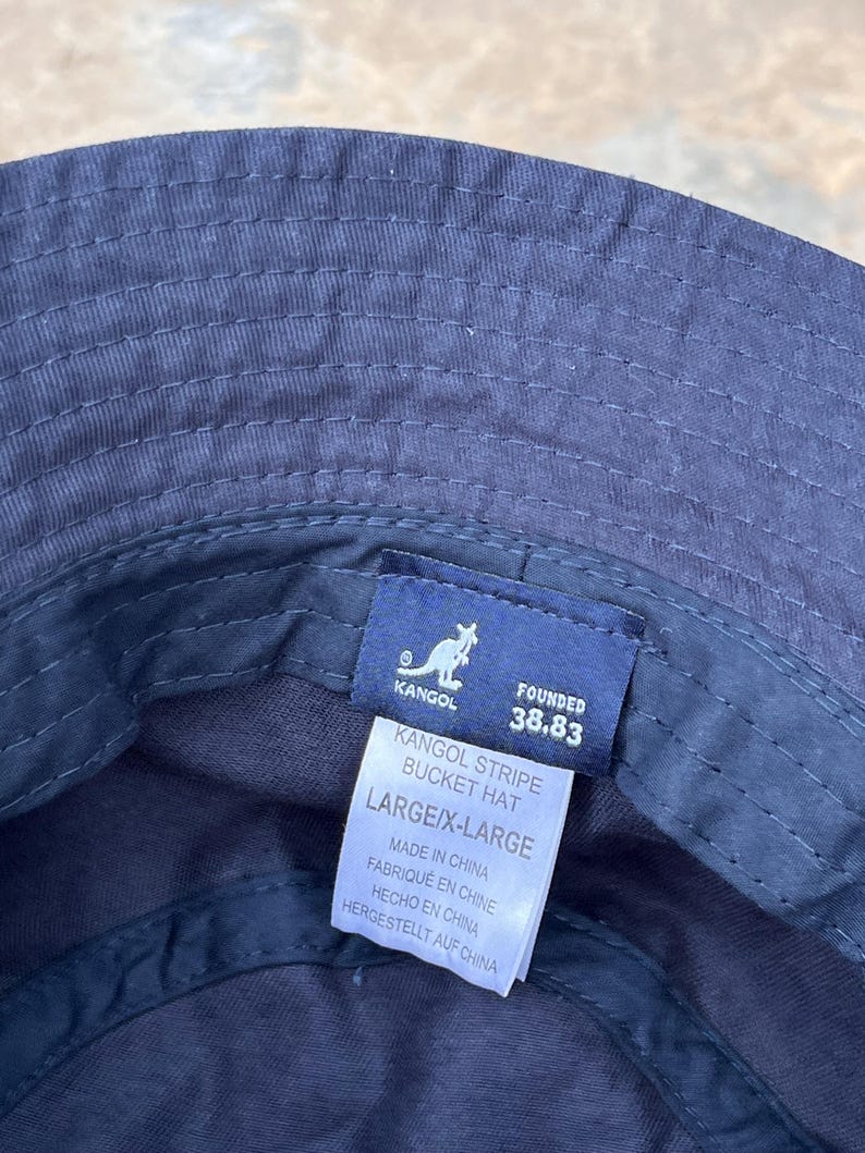May include: Navy blue Kangol Stripe bucket hat, size large/X-large. The hat features a stitched design and a tag with the Kangol logo and text. Made in China.