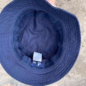 May include: Navy blue bucket hat with a stitched brim. The hat has a tag that reads "LARGE/X-LARGE" and "38.83". The hat is made of a soft material and is designed to be worn outdoors.