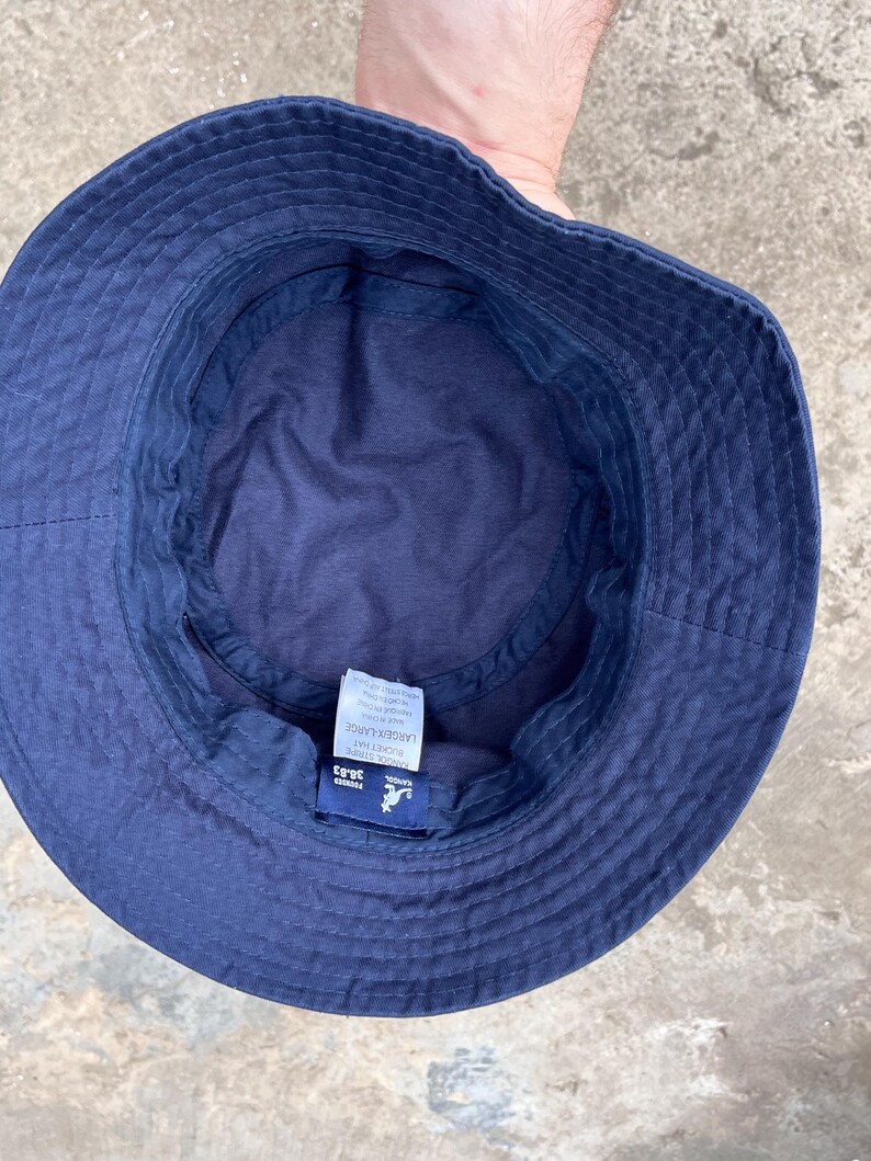 May include: Navy blue bucket hat with a stitched brim. The hat has a tag that reads "LARGE/X-LARGE" and "38.83". The hat is made of a soft material and is designed to be worn outdoors.