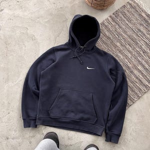 May include: A navy blue hooded sweatshirt with a drawstring hood and a front kangaroo pocket. The Nike logo is visible on the upper left chest. The sweatshirt is made of a soft material.