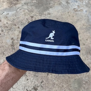May include: Navy blue bucket hat with white stripes and the word "KANGOL" below a kangaroo logo. The hat is made of a soft material and is suitable for casual wear. The hat is a classic style.