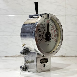 Può includere: Un telegrafo navale vintage con un involucro in metallo color argento. Il quadrante circolare mostra i comandi di velocità e direzione come "Tutta avanti" e "Stop". C'è una maniglia nera in alto. Un oggetto da collezione nautico.