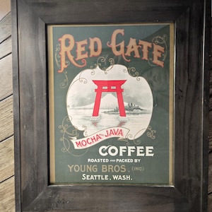 Pode incluir: Anúncio vintage emoldurado para "Red Gate Mocha and Java Coffee" com uma ilustração de um portão torii vermelho. O texto inclui "Roasted and Packed by Young Bros. (Inc.) Seattle, Wash." A moldura é cinza escuro.