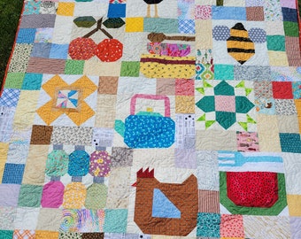 May include: A colourful patchwork quilt featuring a variety of shapes and designs, including a teapot, a chicken, a bee, a cherry, a flower, and an acorn. The quilt is made with a range of fabrics in shades of green, blue, red, yellow, and brown.