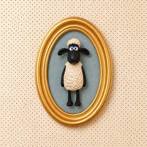 Peut inclure: Une décoration murale en relief représentant un mouton sculpté avec un visage noir, de grands yeux blancs et un corps en laine texturée de couleur crème. La figurine est montée dans un cadre ovale doré sur un fond bleu.