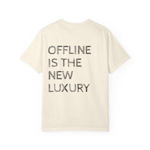 Könnte beinhalten: Cremefarbenes T-Shirt mit dem Aufdruck "OFFLINE IS THE NEW LUXURY" in schwarzen Blockbuchstaben. Das Shirt hat kurze Ärmel und einen Rundhalsausschnitt. Der Text ist auf der Rückseite des Shirts zentriert.