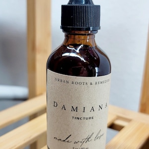 May include: A brown glass bottle with a black dropper top. The label reads "DAMIANA TINCTURE" and "Urban Roots & Remedies." The bottle contains a liquid and is labeled "made with love" and "2 oz / 60 ml."