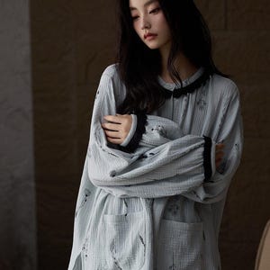 May include: Light blue pajama set with a floral pattern. The long-sleeved top has a black lace trim around the collar and cuffs. The pajama set includes a top with two pockets and matching pants.