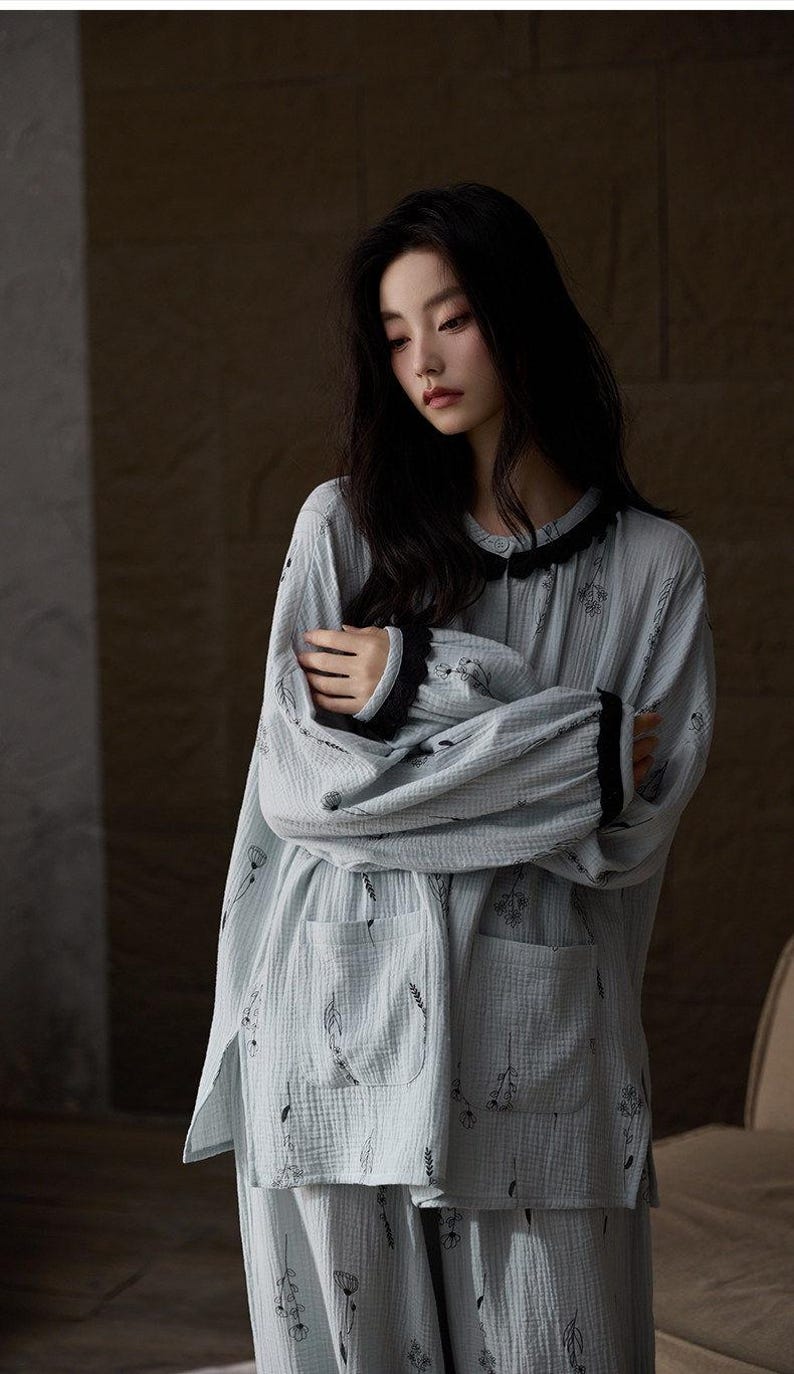 May include: Light blue pajama set with a floral pattern. The long-sleeved top has a black lace trim around the collar and cuffs. The pajama set includes a top with two pockets and matching pants.