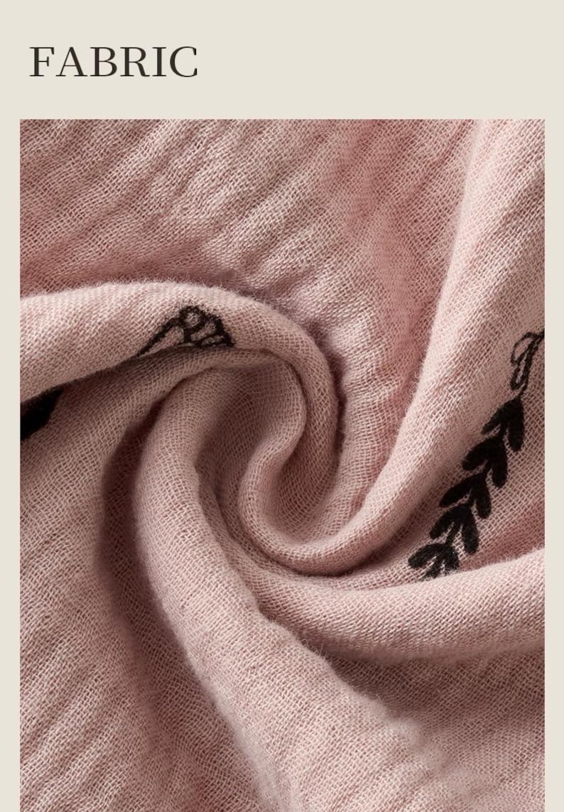 May include: Close-up of a dusty rose fabric with a woven texture. The fabric has a delicate, slightly wrinkled appearance. Black leaf-like designs are printed along the edge. The word "FABRIC" is printed in a serif font at the top.