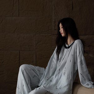 May include: Light blue pajama set with a floral pattern. The long-sleeved top has a black trim around the collar and cuffs. The matching pants are loose-fitting. The fabric appears to be a soft, textured material.