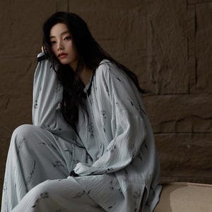 May include: Light blue pajama set with a floral pattern. The long-sleeved top and matching pants are made of a soft, textured fabric. The pajamas are designed for comfort and relaxation.