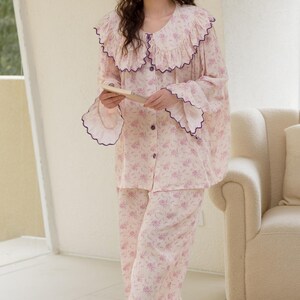May include: A light pink floral pajama set with a ruffled collar and cuffs trimmed in purple. The long-sleeved top has buttons down the front, and the matching pants are wide-legged. The pajamas are made of a soft, lightweight fabric.