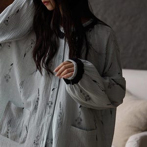 May include: Light blue pajama set with a floral pattern. The long-sleeved top has a button-down front, two pockets, and black trim on the cuffs and collar. The fabric appears soft and lightweight.
