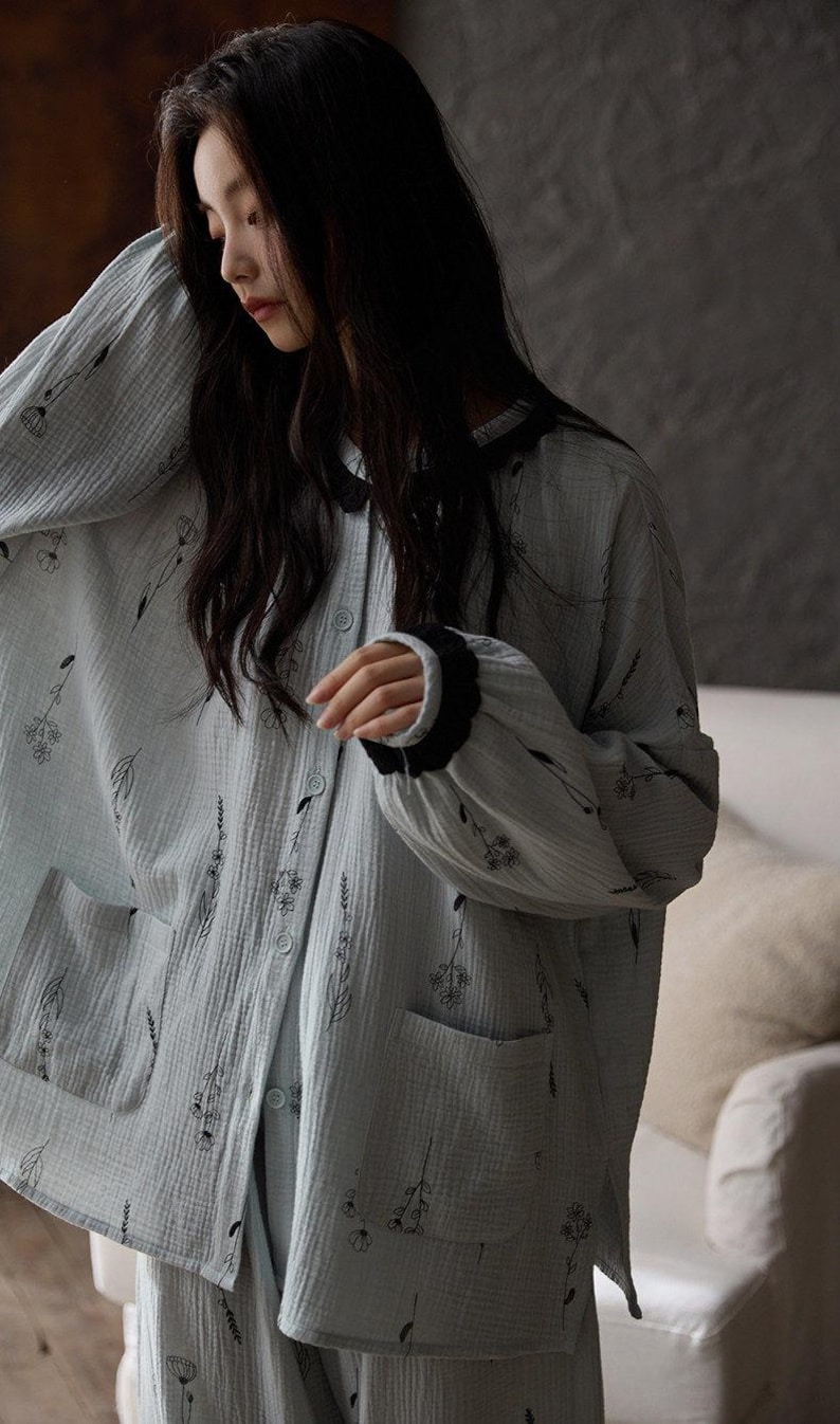 May include: Light blue pajama set with a floral pattern. The long-sleeved top has a button-down front, two pockets, and black trim on the cuffs and collar. The fabric appears soft and lightweight.
