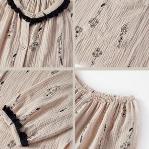 May include: Beige pajama set with a floral pattern. The top has a round collar with black lace trim and button closure. The long-sleeved top and pants feature a delicate black floral design. The fabric has a textured, crinkled appearance.