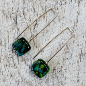May include: A pair of silver dangle earrings with square green and black glass beads. The beads have a marbled pattern.