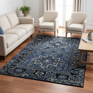 May include: A rectangular, blue area rug with a geometric pattern. The rug features a central design in shades of blue, gray, and cream, framed by a black border. The rug is placed on a hardwood floor in a living room setting.