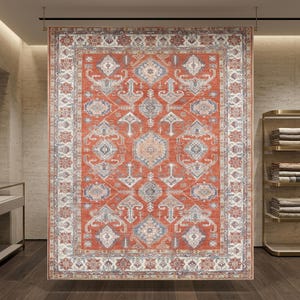 May include: A rectangular area rug featuring a vibrant terracotta orange background with a symmetrical pattern of intricate geometric shapes, floral motifs, and diamond medallions in shades of cream, slate blue, and muted gray with a wide border.