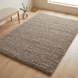 May include: A rectangular area rug featuring a thick, high-pile shag texture in a solid neutral beige color. The rug is constructed with dense, soft fibers that create a plush, uneven surface appearance across the entire top of the floor covering.