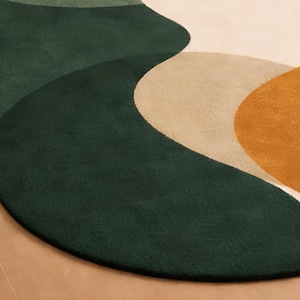May include: A round rug with a modern design. The rug features a combination of colors, including dark green, light green, beige, and mustard yellow. The design has a flowing, abstract pattern.