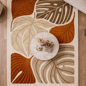 May include: A rectangular rug featuring a leaf pattern in shades of brown, beige, and orange on a cream backdrop. A round marble coffee table sits on the rug.
