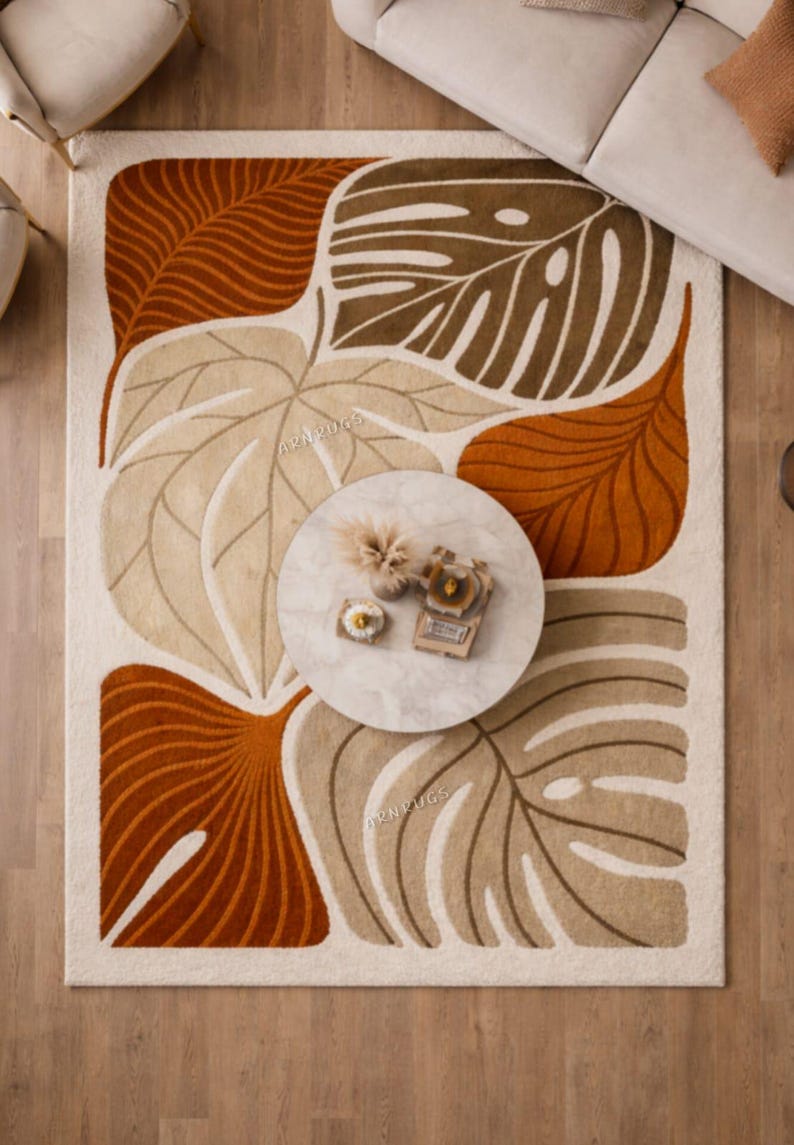 May include: A rectangular rug featuring a leaf pattern in shades of brown, beige, and orange on a cream backdrop. A round marble coffee table sits on the rug.
