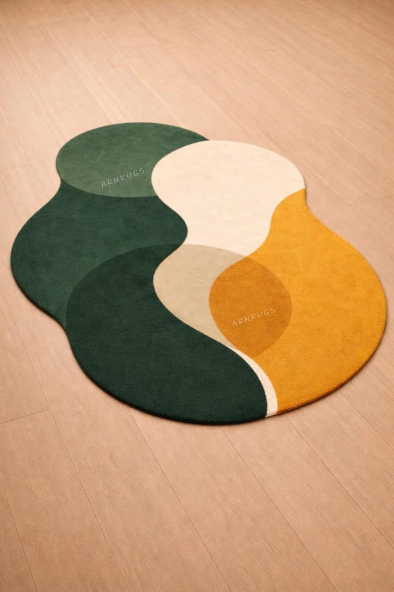 May include: A modern, abstract area rug with a unique, organic shape. The rug features overlapping sections of dark green, beige, cream, and mustard yellow. The text "ARNRUGS" is visible on the rug.