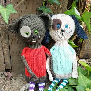 May include: Two knitted plush toys shaped like dogs. The dog on the left is brown with a red shirt and purple and white striped trousers. The dog on the right is white with a blue shirt and green and white striped trousers.