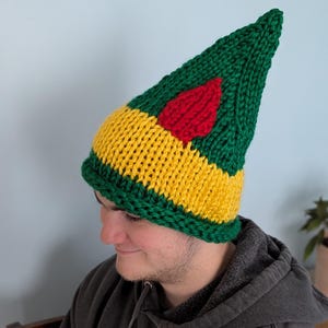 May include: A green, yellow, and red knitted elf hat with a pointed top. The hat has a red heart design on the front.